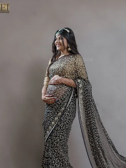 A side profile showcasing the beautiful drape of the sheer black saree over the baby bump.