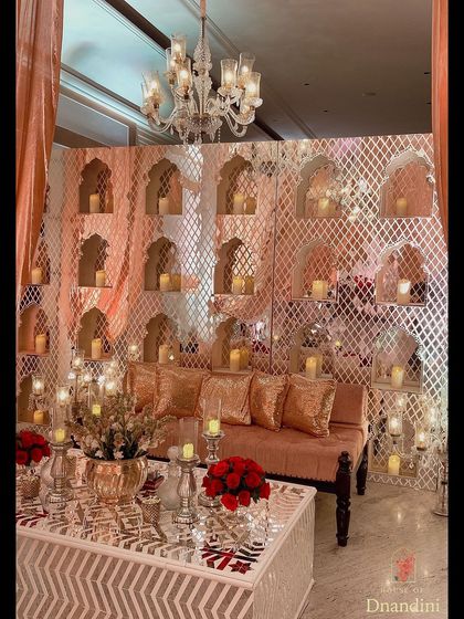 A lounge area from the traditional sangeet, featuring a backdrop of niches filled with candles. The coffee table has a mirrored top with thikri work, reflecting the warm candlelight beautifully.