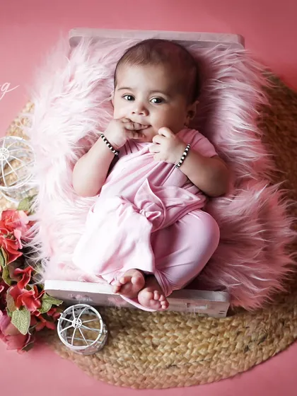 A full-length shot of a three-month-old baby in a pink outfit, curiously nibbling on her fingers. These are the little details we love.