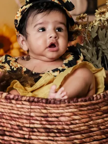A curious baby girl peeking out of a basket in our sunflower setup.