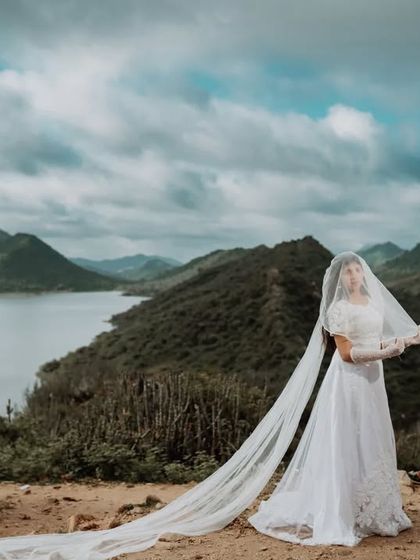 A fairytale-inspired portrait with the bride-to-be in a white gown and long veil, set against the dramatic backdrop of Udaipur's lakes and mountains.