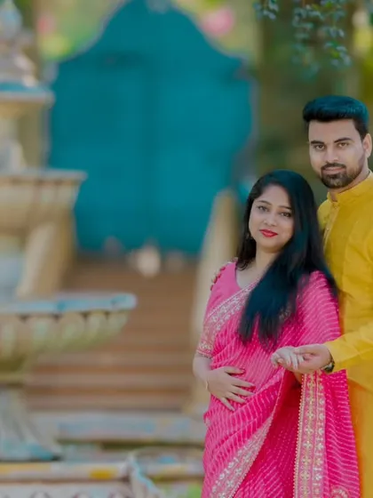 A lovely pre-wedding photo of a couple in a garden setting with a fountain. The groom's yellow kurta and the bride's pink saree are a classic combination.