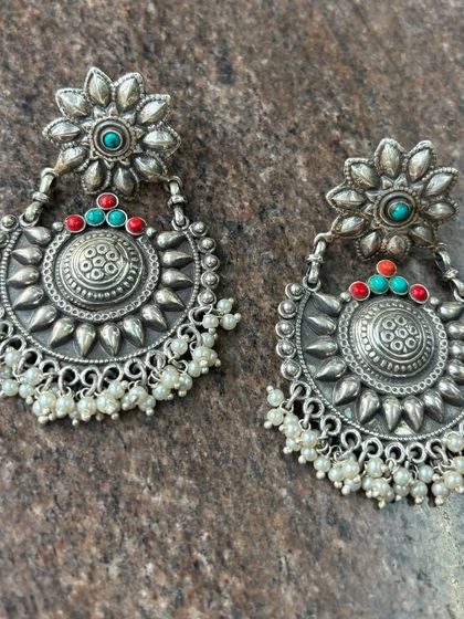 Beautifully detailed oxidised silver chandbali earrings. These feature a floral top, a sun-like central motif, and clusters of pearl drops.