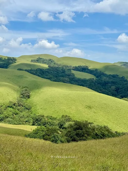 The classic rolling green hills of the Western Ghats under a bright blue sky, seen from the Bandaje Falls trail.
