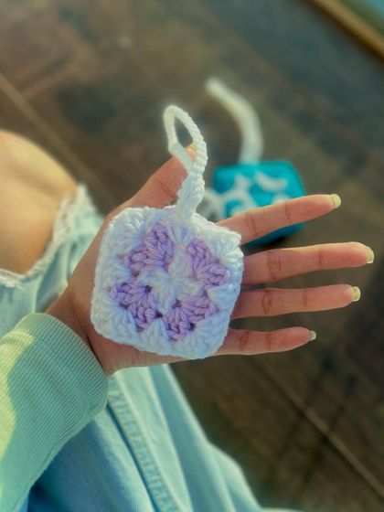 A soft, lilac and white granny square pouch, perfectly sized for AirPods. The handmade construction provides a cushioned layer of protection, and the pastel colors give it a gentle, aesthetic look.