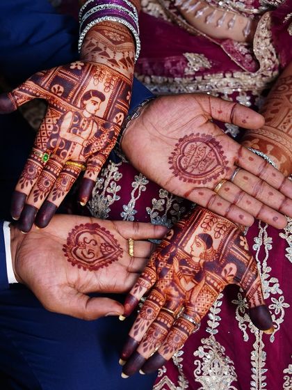 A beautiful shot of the bride and groom's hands, showcasing their coordinated mehendi designs. Her hands feature portraits, while his has their initials in a heart.