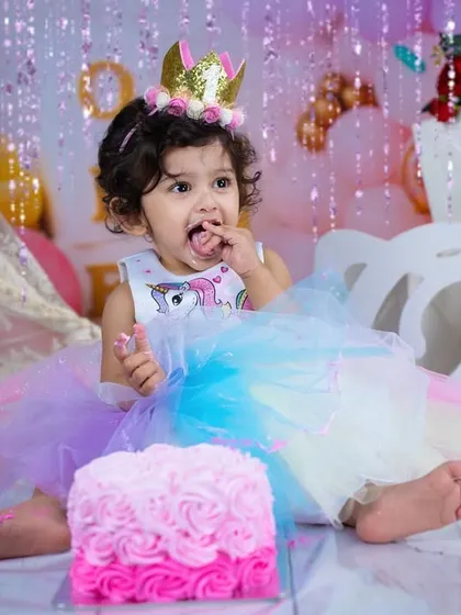 A moment of delicious discovery during a unicorn-themed cake smash. The colorful dress and pink cake create a perfectly magical birthday scene.