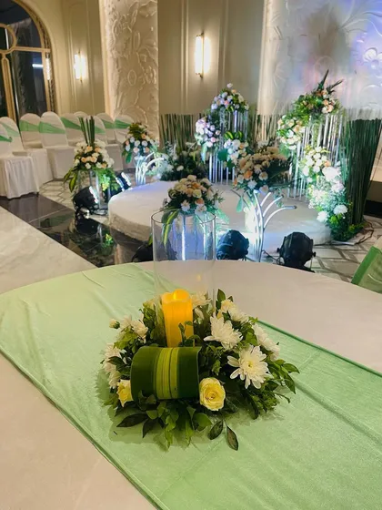 A table centerpiece from the green and white engagement setup. The candle adds a warm glow, complementing the fresh floral arrangement.
