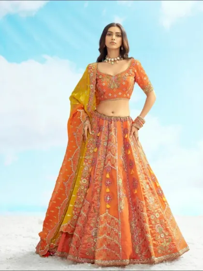 A full-length view of the stunning orange lehenga with its contrasting yellow dupatta. This is a perfect, eye-catching outfit for any celebration.