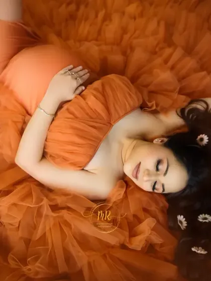 An artistic overhead shot with the mother-to-be lying on a bed of orange tulle. Her hair is decorated with daisies, creating a whimsical and beautiful fine art pregnancy portrait.