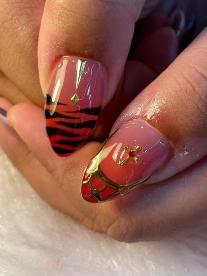 A close-up look at our detailed nail art. This nail features a red and black tiger print base, overlaid with a delicate gold web and a tiny cross charm, showing how we layer elements to create a unique story on each finger.