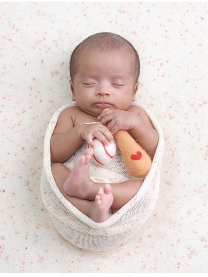 A home run of a photo. This newborn is posed with a miniature baseball and bat, a perfect theme for a sports-loving family.