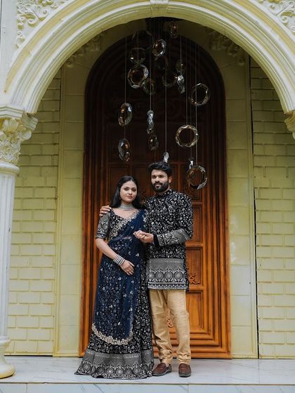 A grand, full-length portrait of a couple in front of a large arched doorway with modern light fixtures.