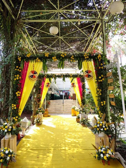 A vibrant yellow-themed entrance for a Haldi ceremony. The pathway is lined with colorful drapes and floral arrangements, creating a festive and cheerful welcome for guests.