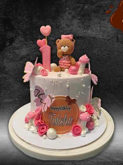 A sweet and pretty first birthday cake featuring a cute fondant teddy bear. The cake is decorated with pink butterflies, flowers, and mushrooms, creating a lovely woodland scene.