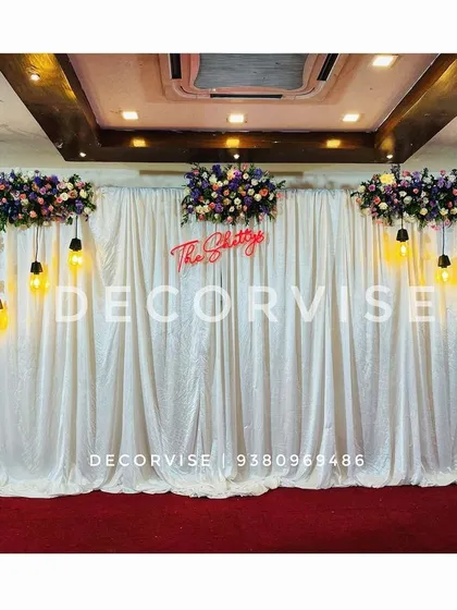 I designed this reception stage with a touch of glamour, using a floor-to-ceiling white sequin curtain for a sparkling effect. The look is balanced with rich floral arrangements and vintage-style hanging bulbs, with a custom neon sign of the family name adding a personal touch.