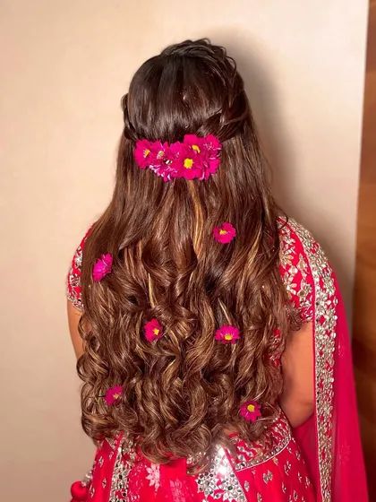 A half-updo with fresh pink flowers scattered through the curls, a perfect look for a Haldi or Mehendi.