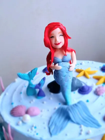 A close-up of the hand-sculpted mermaid topper on the buttercream cake.