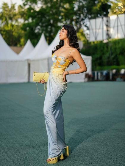 A full-length shot from an editorial shoot, where the model's glamorous waves complement her designer gown and the outdoor setting.