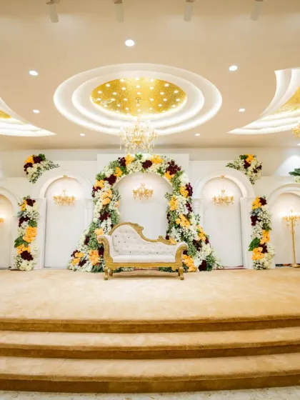 This is a classic and elegant wedding stage, featuring a beautiful floral arch with rich colors and a royal diwan-style sofa. The design combines traditional aesthetics with luxurious touches like mini chandeliers, perfect for a timeless wedding ceremony.
