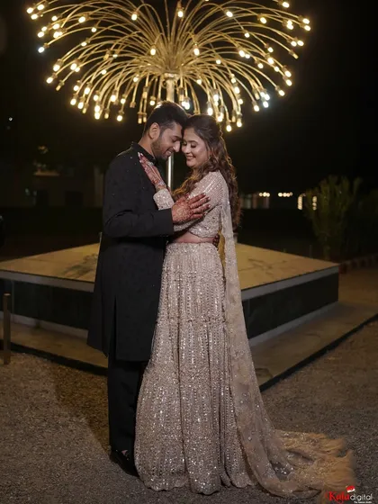 A wide shot of the couple under a beautiful light installation, the bride's sequined lehenga sparkling in the night.