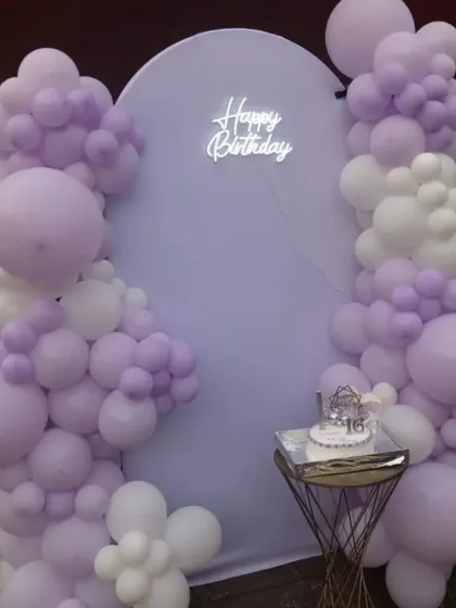 A dreamy sweet 16 setup in pastel lavender. The simple arch backdrop is framed by a beautiful balloon garland, creating a soft and elegant photo corner.