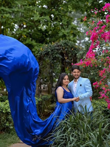 A beautiful shot of a flowing blue gown amidst the pink flowers and greenery of the garden.