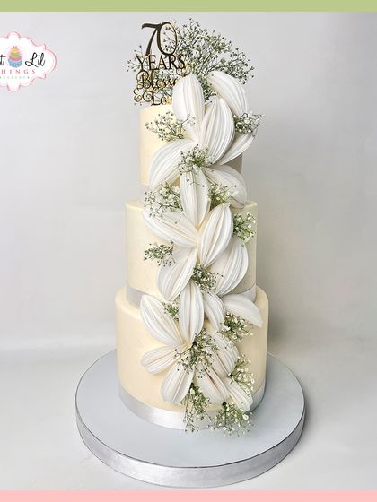 A breathtaking three-tiered cake celebrating 70 years of love. This elegant design features a cascade of large, handcrafted white sugar flowers, creating a timeless and sophisticated look.