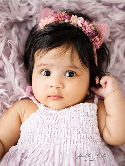 A close-up of this adorable baby, focusing on her curious expression and the cute floral headband. Her wide eyes are simply captivating.