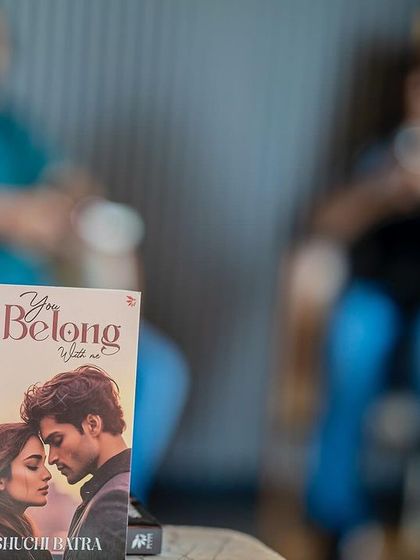 A close-up of the book "You Belong with Me" with the event's audience blurred in the background, set in the stylish Sapphire by Unicorn cafe.