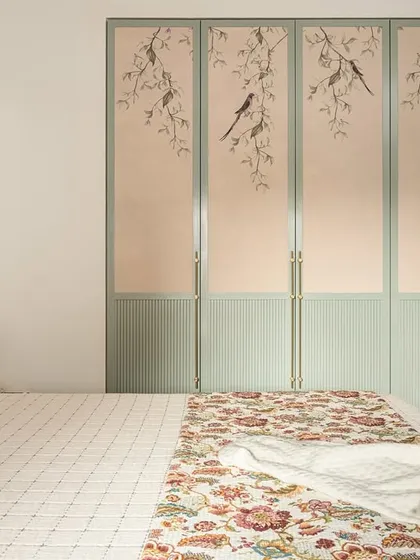 For the 'Palaash' master bedroom, we designed this serene wardrobe featuring custom wallpaper with a delicate bird and branch motif. The soft sage green PU finish and elegant handles create a piece that is both storage and art.