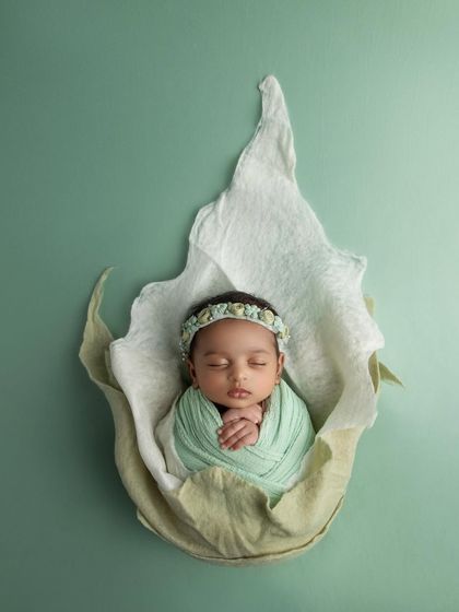 A slightly different pose within the flower prop, this image showcases the baby's delicate hands and the beautiful, handcrafted details of her headband.