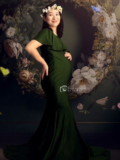 A whimsical portrait with a mom-to-be wearing a floral crown, set against a dark, moody floral wreath background.