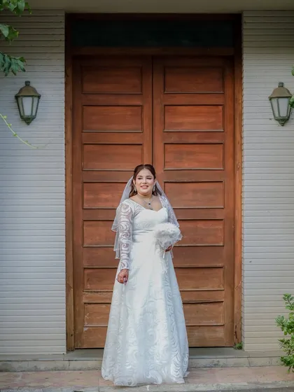 A full-length portrait of a smiling Christian bride in her beautiful white gown, holding a bouquet and ready for her ceremony.