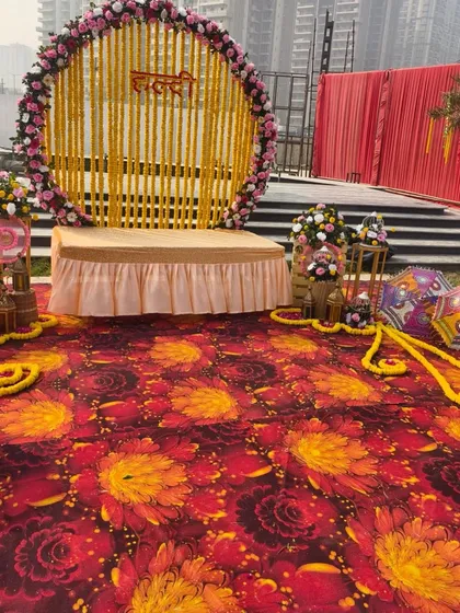 The main seating area for the Haldi ceremony, with a traditional marigold backdrop and a colorful printed carpet on the floor.
