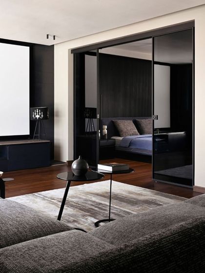 The upper floor of Villa Aish was conceived as a private studio apartment. This view shows the living area transitioning into the bedroom through smoked glass sliding doors, creating a sophisticated and moody suite with a darker, more intimate material palette.