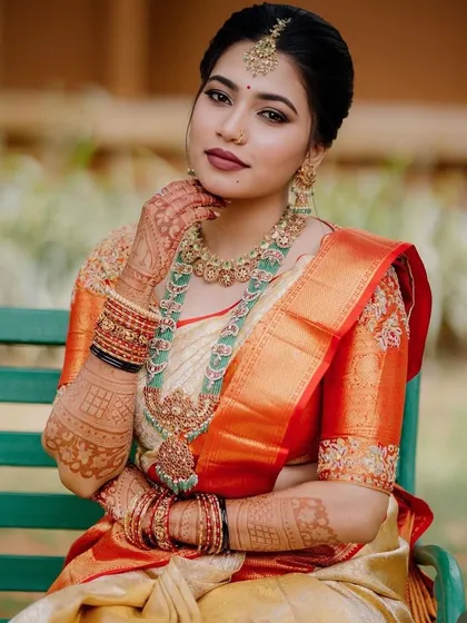 A beautiful portrait of an AMAIRA bride. Her custom orange blouse with subtle zardozi work perfectly matches the border of her cream-colored wedding saree.