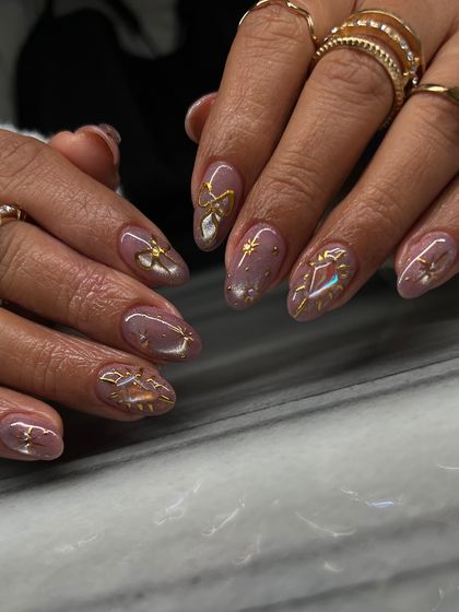 A beautiful set featuring a shimmery mauve base with intricate, hand-painted gold celestial designs. Each nail has a unique charm, from stars to bows.