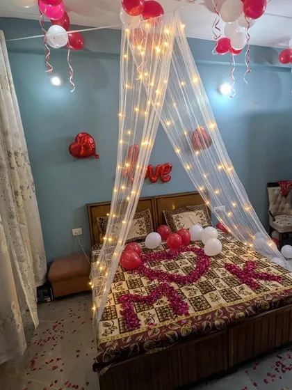 A full view of the romantic room makeover, with a fairy light canopy, balloons, and rose petals on both the bed and the floor.