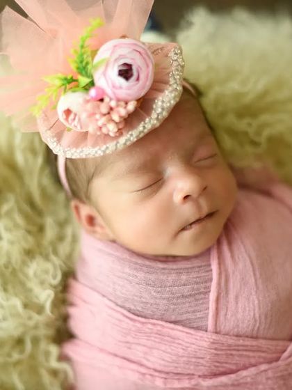 A touch of vintage charm with this tiny fascinator-style hat. The baby is wrapped in a soft pink swaddle.