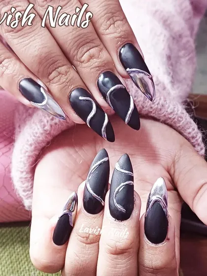 A striking and unique design featuring long, stiletto-shaped nails. The matte black base is contrasted with raised, 3D silver chrome swirls and accents, creating a futuristic and textural look that is both dark and glamorous.