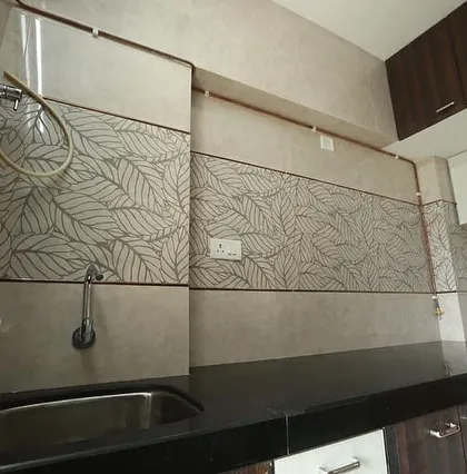 This kitchen backsplash features a combination of plain and leaf-patterned tiles, creating a subtle design accent. The black granite countertop provides a durable and easy-to-maintain work surface.