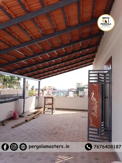 A work-in-progress shot of a Mangalore tile pergola on a terrace. The project includes a custom-designed metal gate with a peacock motif, showcasing our ability to integrate artistic details into our structures.