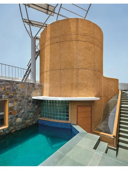 Sustainability and function merge in this rooftop design. The splash pool is flanked by a staircase and a cylindrical core finished in hand-crafted stone-grit plaster, which also supports the solar panels. Rainwater is harvested from the curved roof and channeled into a storage system, showcasing a design where every element serves multiple purposes.