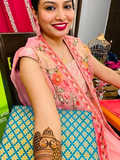 A happy client showing her arm mehndi which features a beautiful peacock design at the top.