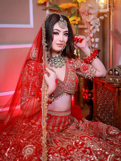 A full seated portrait where the bride is looking directly at the camera, showcasing her confidence and the beautiful red lehenga.