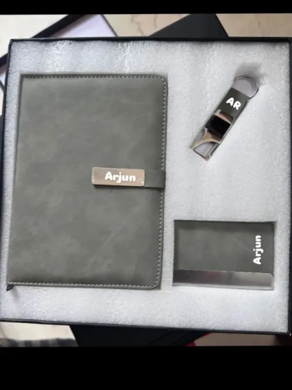A complete corporate gift set including a personalized grey diary, a metal card holder, and a keychain, all engraved with the name 'Arjun'.