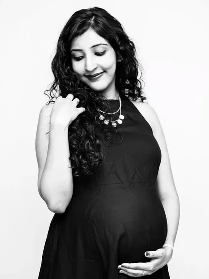 A classic black and white portrait of a mom-to-be, capturing a quiet, contemplative moment. The simple black dress and soft lighting create a timeless feel.
