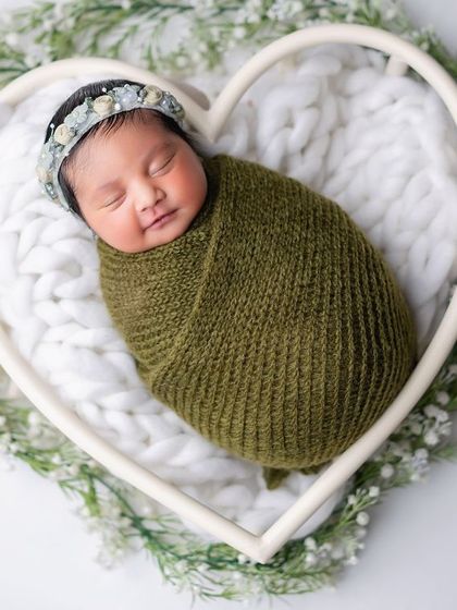 A newborn baby nestled in a heart-shaped basket, surrounded by baby's breath. A perfect way to show your love.