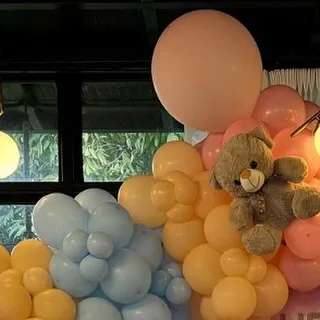 A close-up of the pastel balloon arrangement, showing a small grey teddy bear nestled within the blue and pink clusters.
